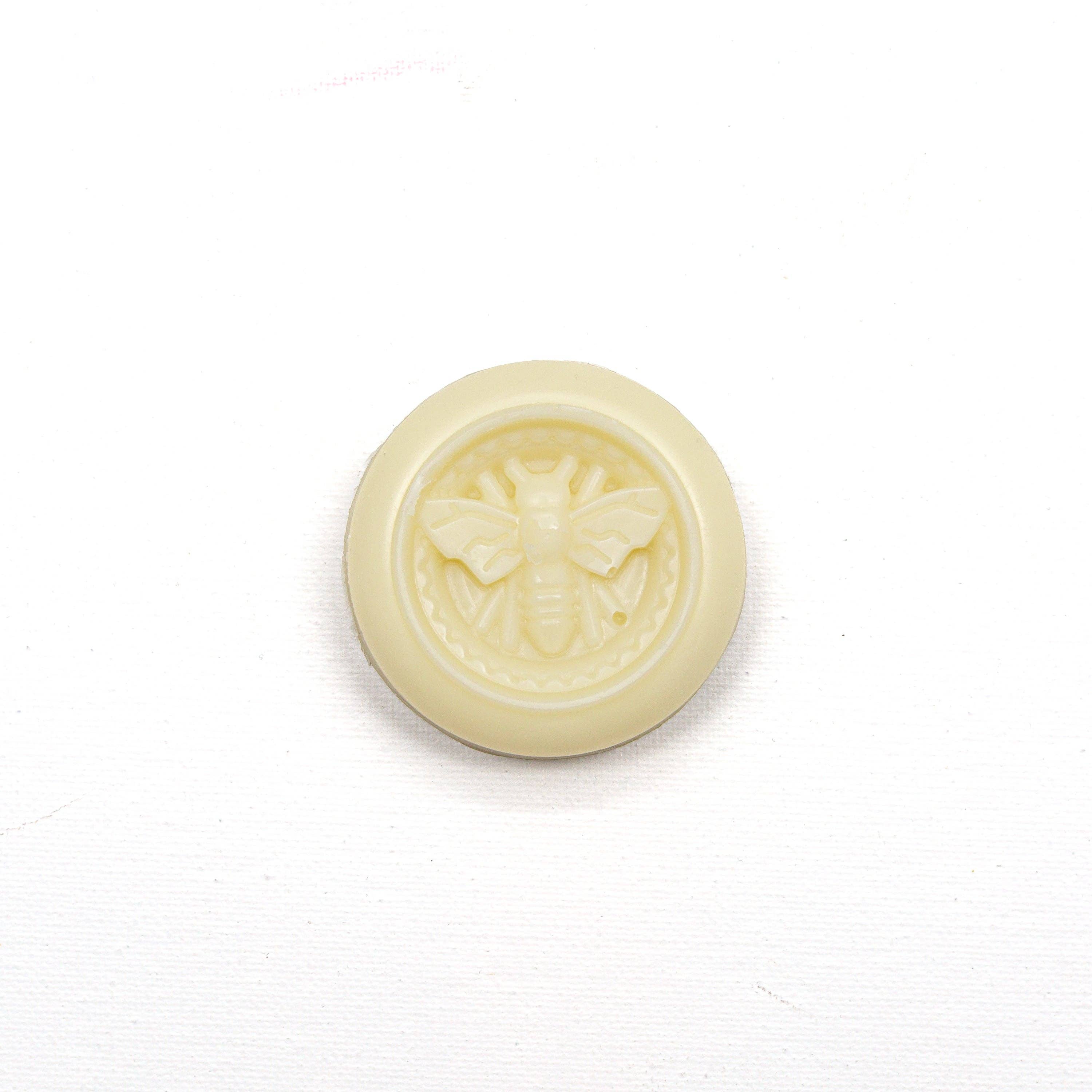 Round white beeswax object with a bee design on a white background