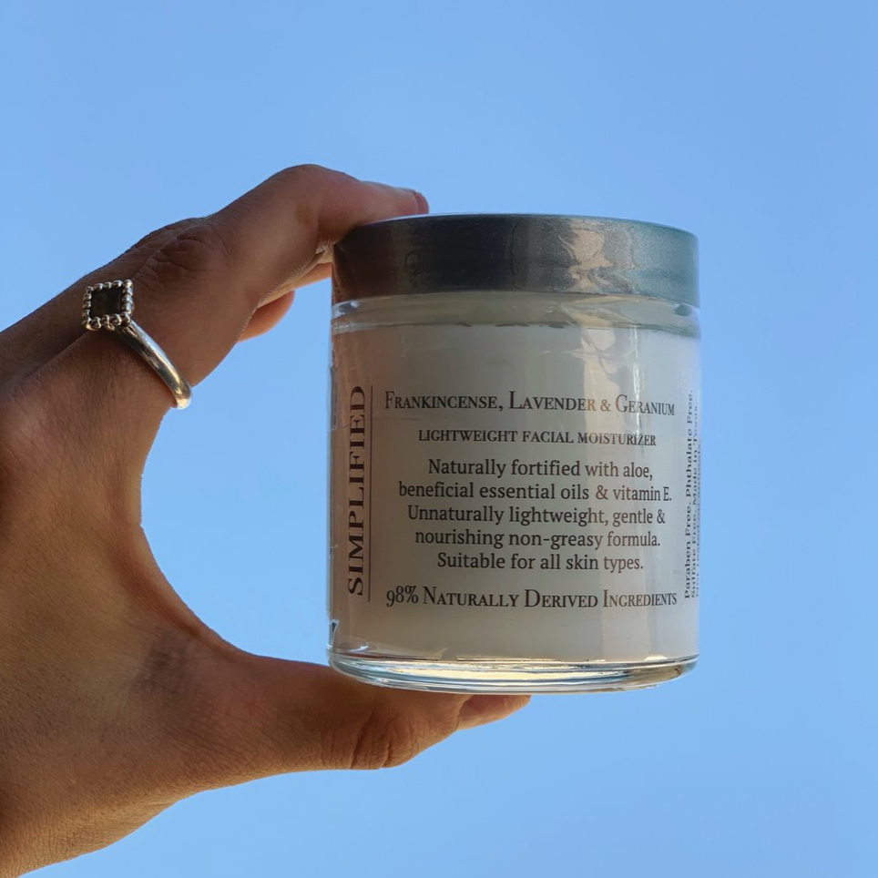 Hand holding a jar of Simplified skincare facial moisturizer against a clear blue sky