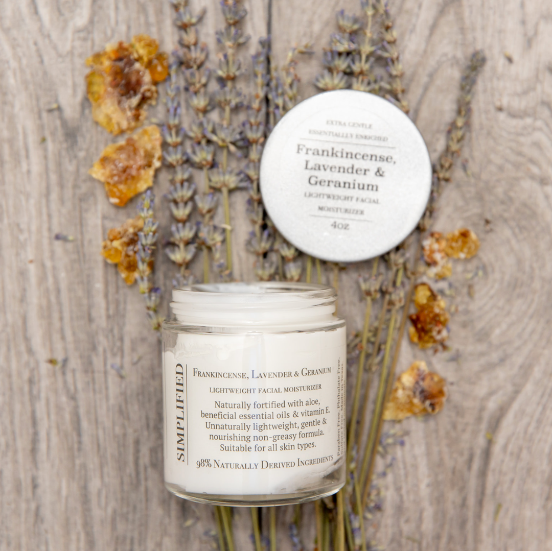 Facial moisturizer jar with lid on a wooden surface with dried flowers and writing Frankincense Lavender Geranium