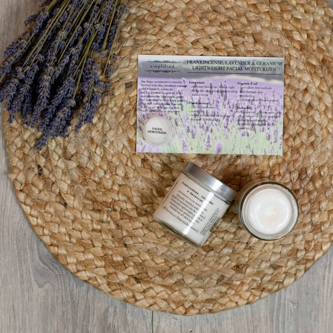 Two jars of facial moisturizer and a card on a woven mat with lavender flowers.